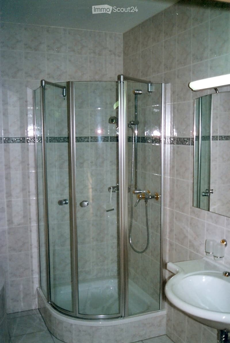 Bathroom with glass shower enclosure, white sink, mirror, and tiled walls.