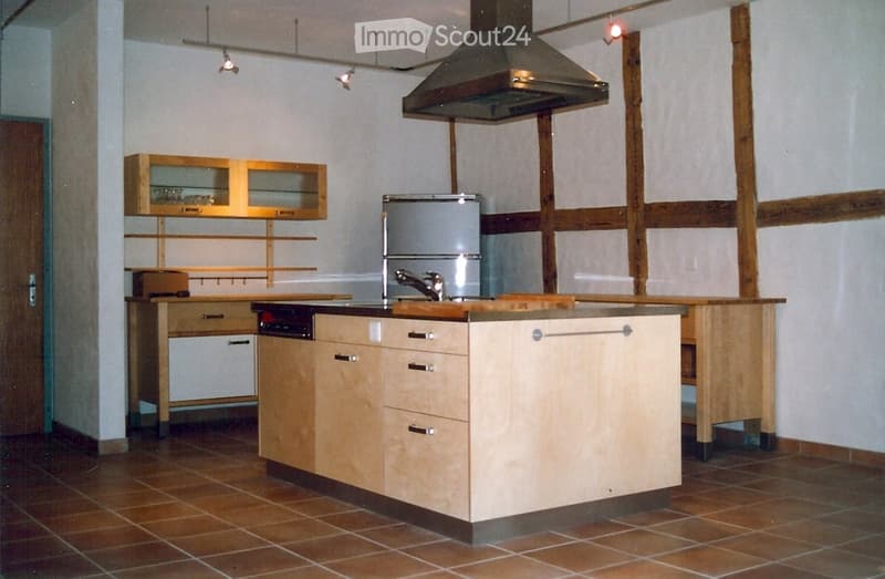 modern kitchen with wooden cabinets, tiled floor, stainless steel appliances, wooden beams, open shelves, and a central island with a sink and faucet