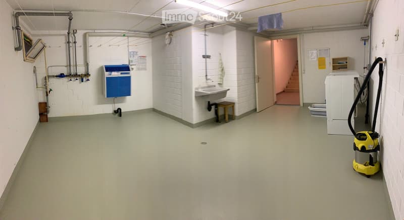 Utility room with white brick walls, a sink, a small wooden stool, a washing machine, a vacuum cleaner, an air conditioning unit, and a small screen mounted on the wall.