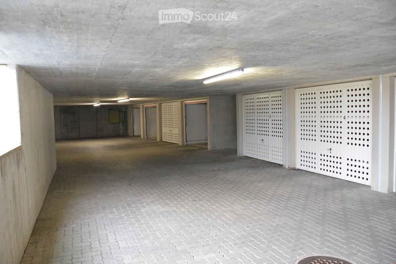 Underground parking area with concrete walls and ceiling, tiled floor, and several closed garage doors.