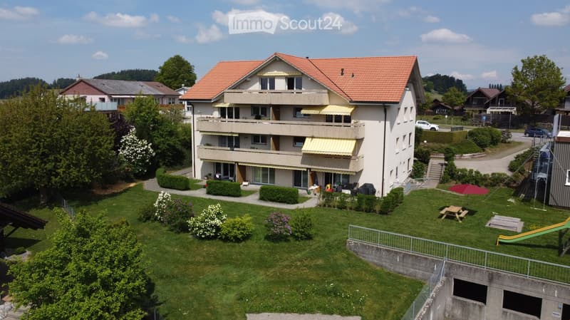 Two-story house with red-tiled roof, multiple balconies, and a well-maintained garden with a picnic table, slide, and outdoor seating.