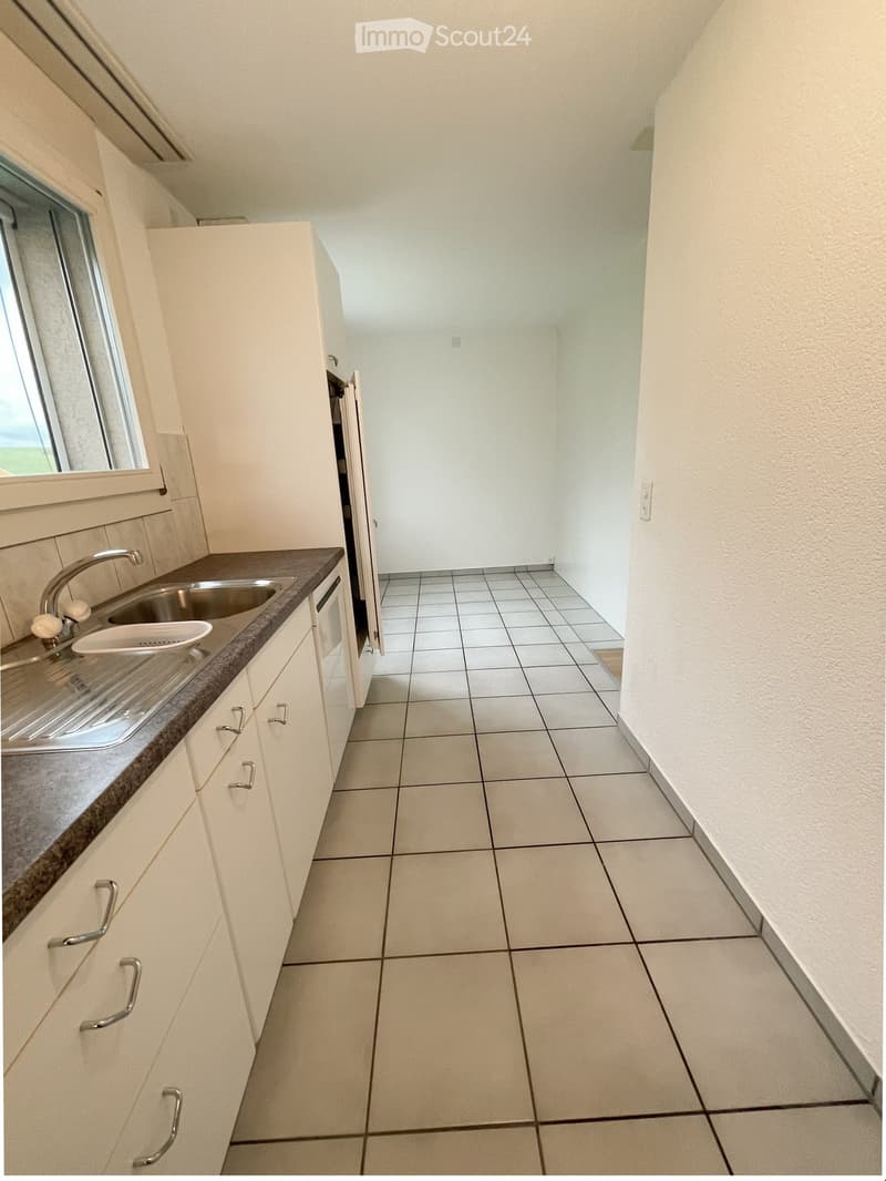 Empty kitchen with white cabinets, tiled floor, and a stainless steel sink.