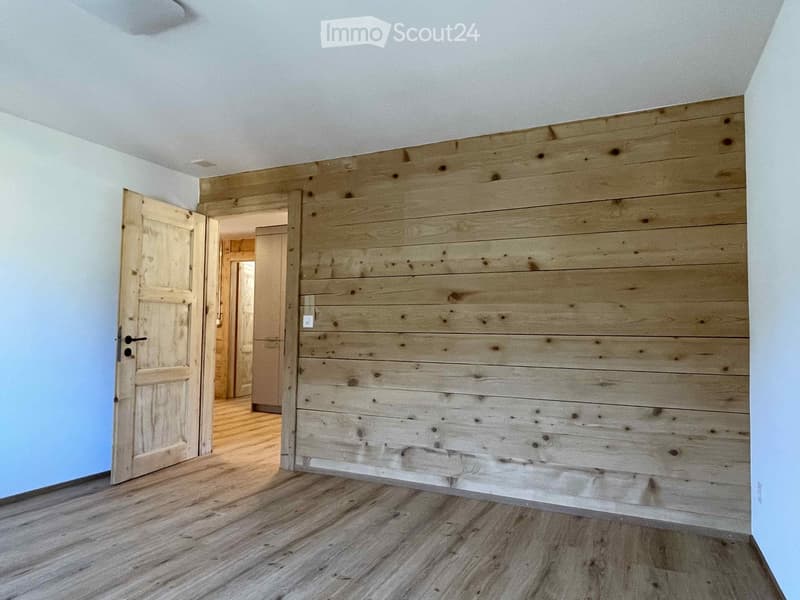 Empty hallway with wooden plank wall, light blue walls, and wooden floor. No furniture or equipment visible.