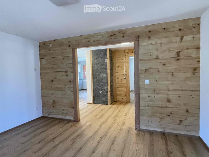 Empty room with wooden flooring and exposed wooden walls, featuring an open doorway leading to another room.