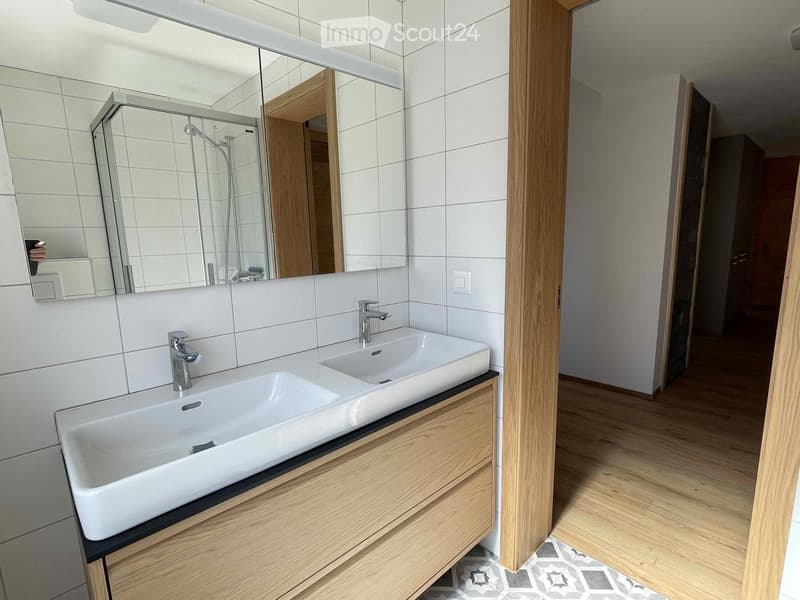 Modern bathroom with a double sink, wooden cabinet, large mirror, and glass shower enclosure.