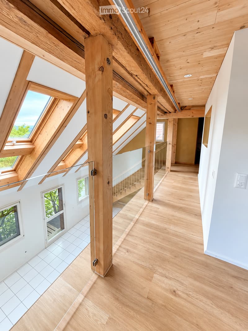 Bright, airy hallway with wooden beams and flooring, large windows, and a staircase leading upwards.