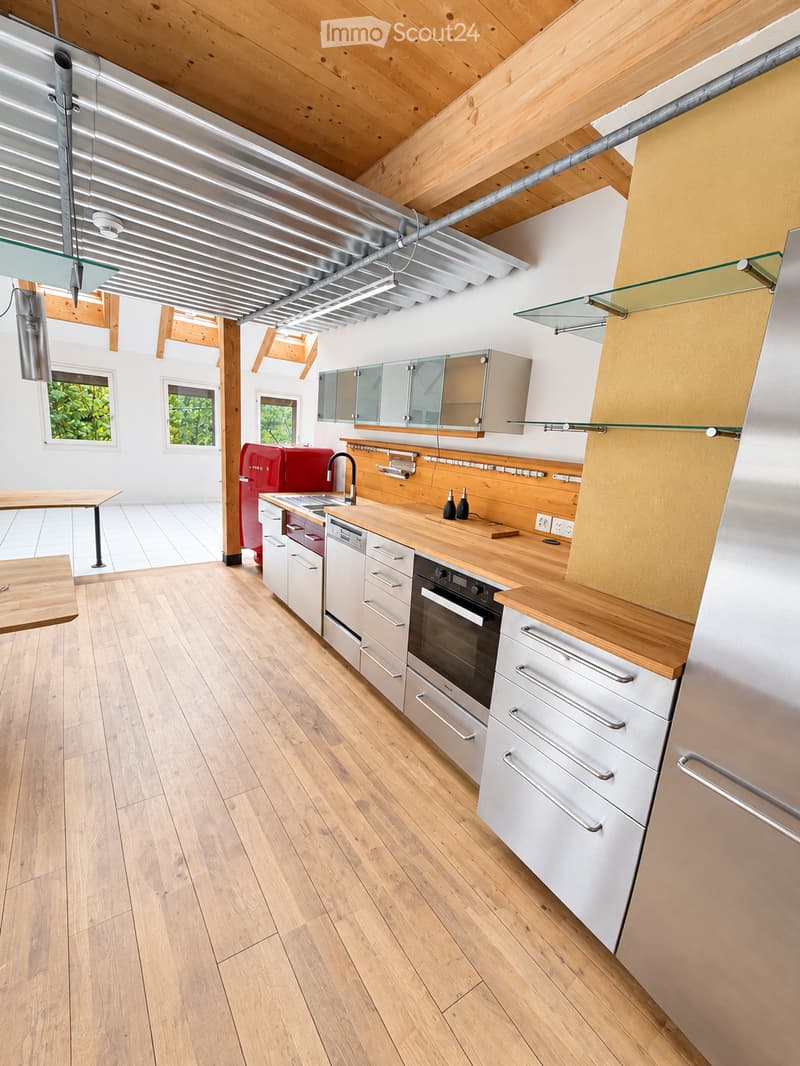 Modern kitchen with wooden flooring, white cabinets, stainless steel appliances, and a red refrigerator. Features include a wooden countertop, glass shelves, and a small dining table.