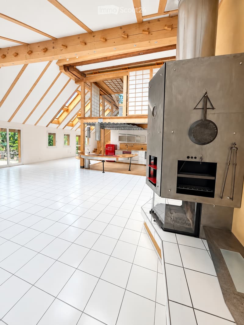Open-plan space with white tiled floor, high wooden ceiling beams, large windows, and a modern kitchen area with cabinets, a table, and an oven.