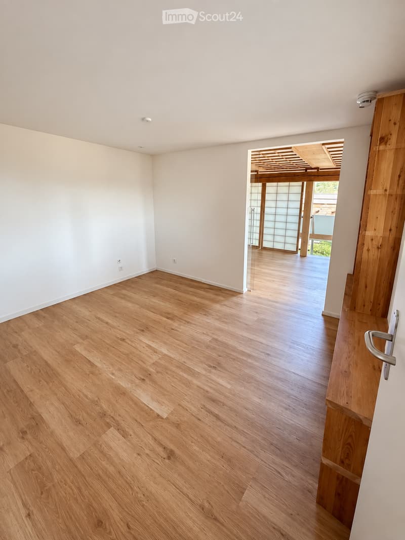 Empty room with light wooden flooring and white walls, featuring a sliding glass door leading to an outdoor area.