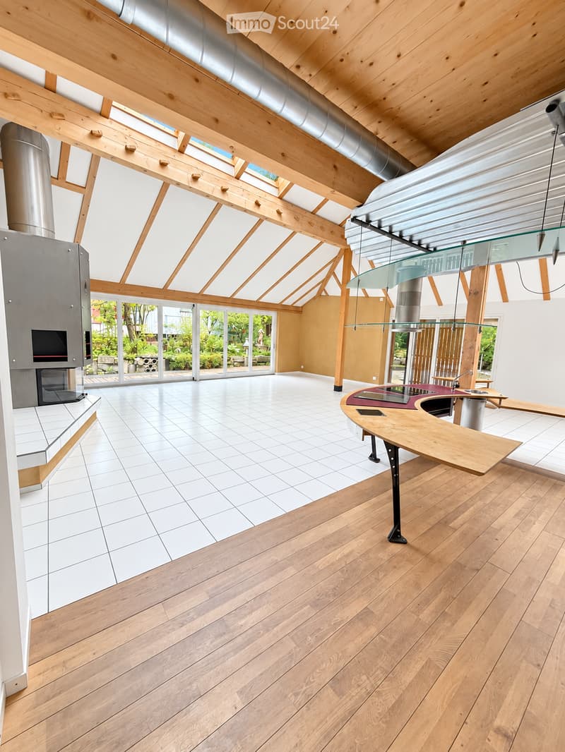Open-plan living and dining area with exposed wooden beams, large skylights, and a modern kitchen island with a sink.