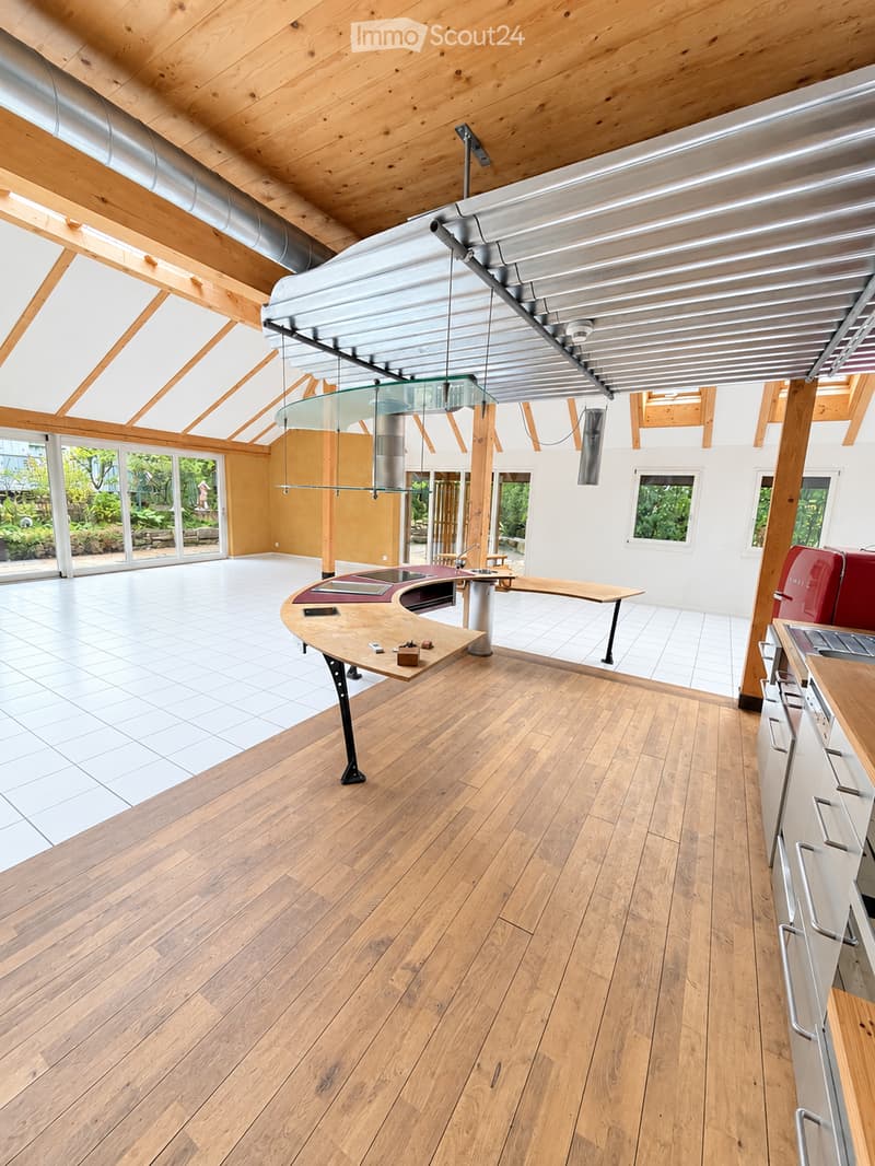 Modern kitchen with wooden flooring, island, cabinets, and a sink area. Large windows and a skylight provide natural light.