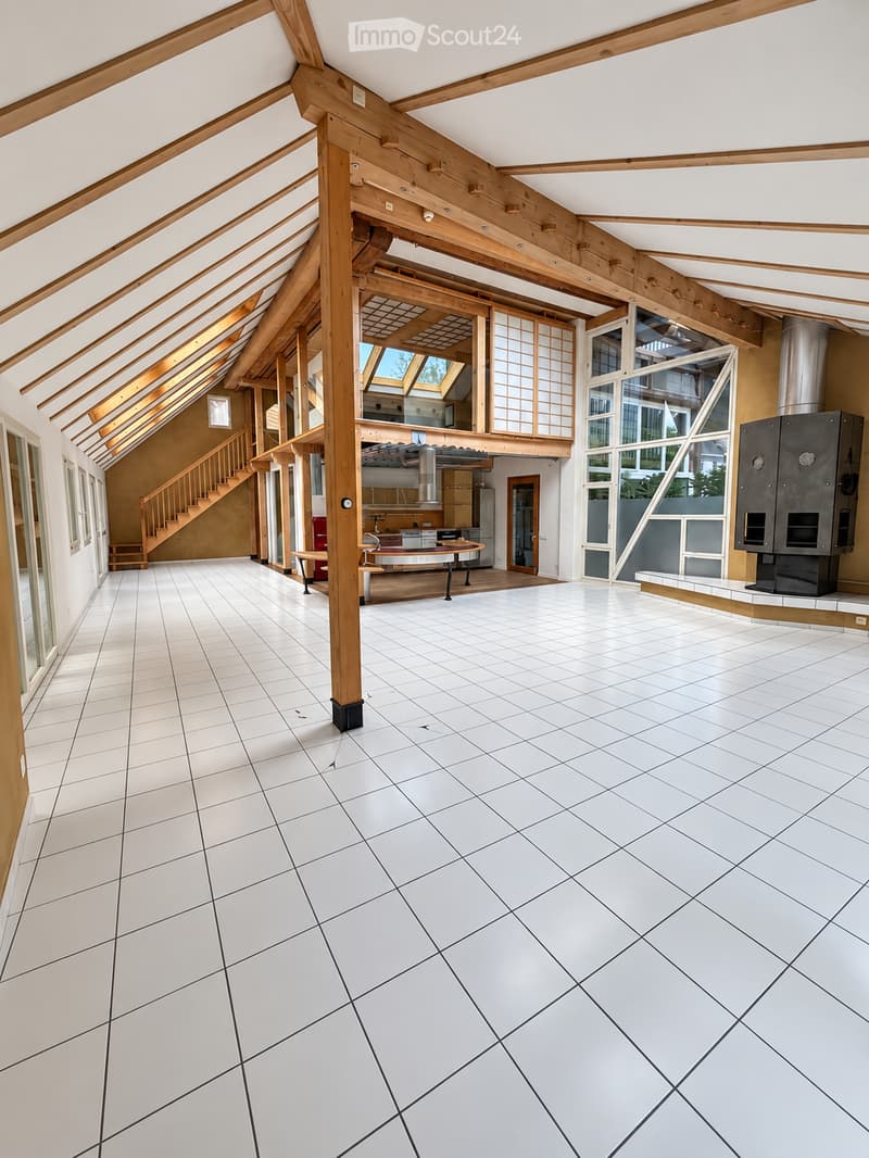 Bright, open room with white tiled flooring, wooden beams, and large windows. The space is empty, with no furniture or furnishings visible.