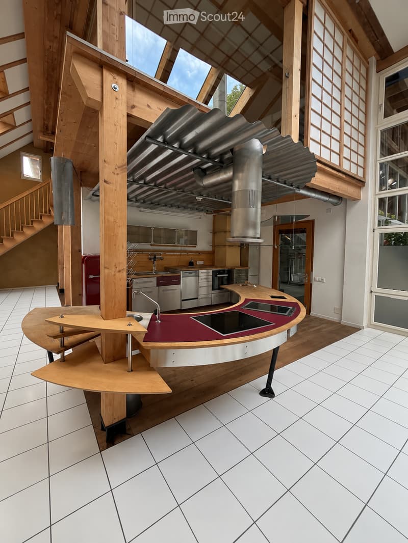 Modern kitchen with white tiled flooring, wooden beams, stainless steel appliances, and a central island with a red countertop and built-in sink.
