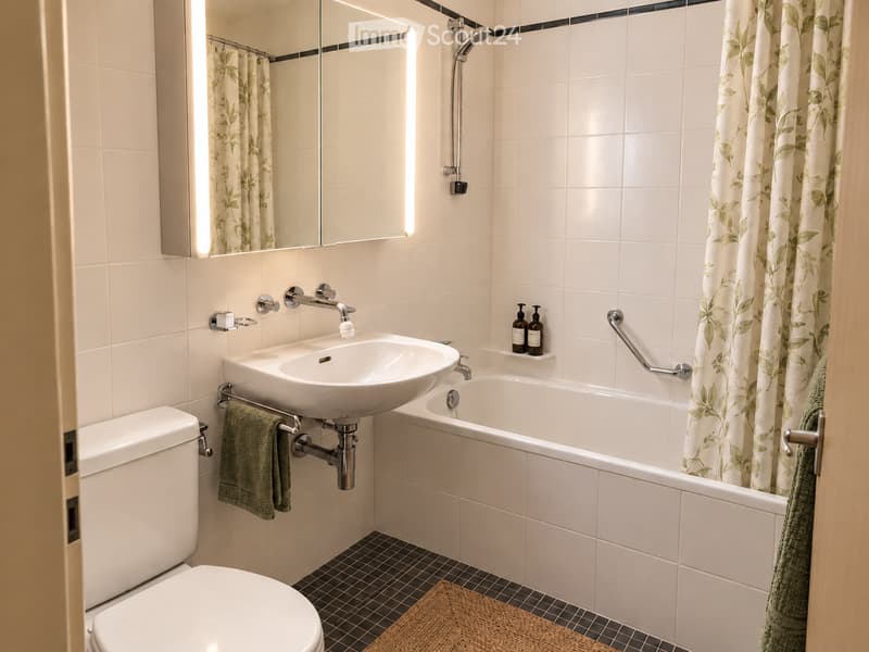 Modern bathroom with white tiles, a bathtub, a sink, a toilet, a mirror, and a shower curtain with a leafy pattern.