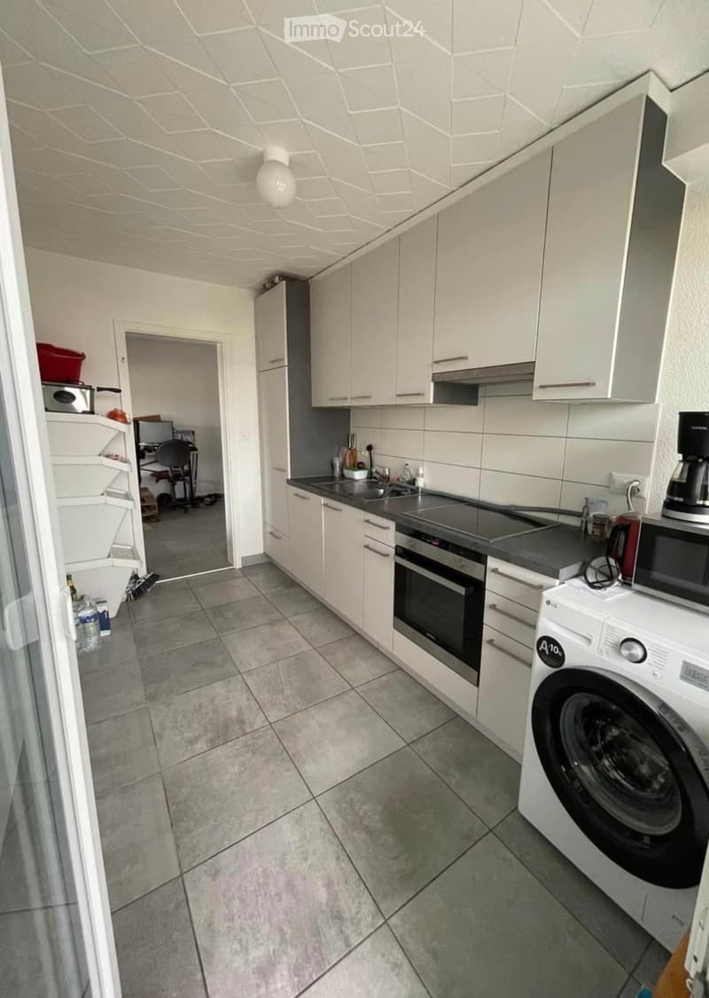 Modern kitchen with white cabinets, stainless steel appliances, and tiled floor. Includes an oven, washing machine, microwave, and sink.