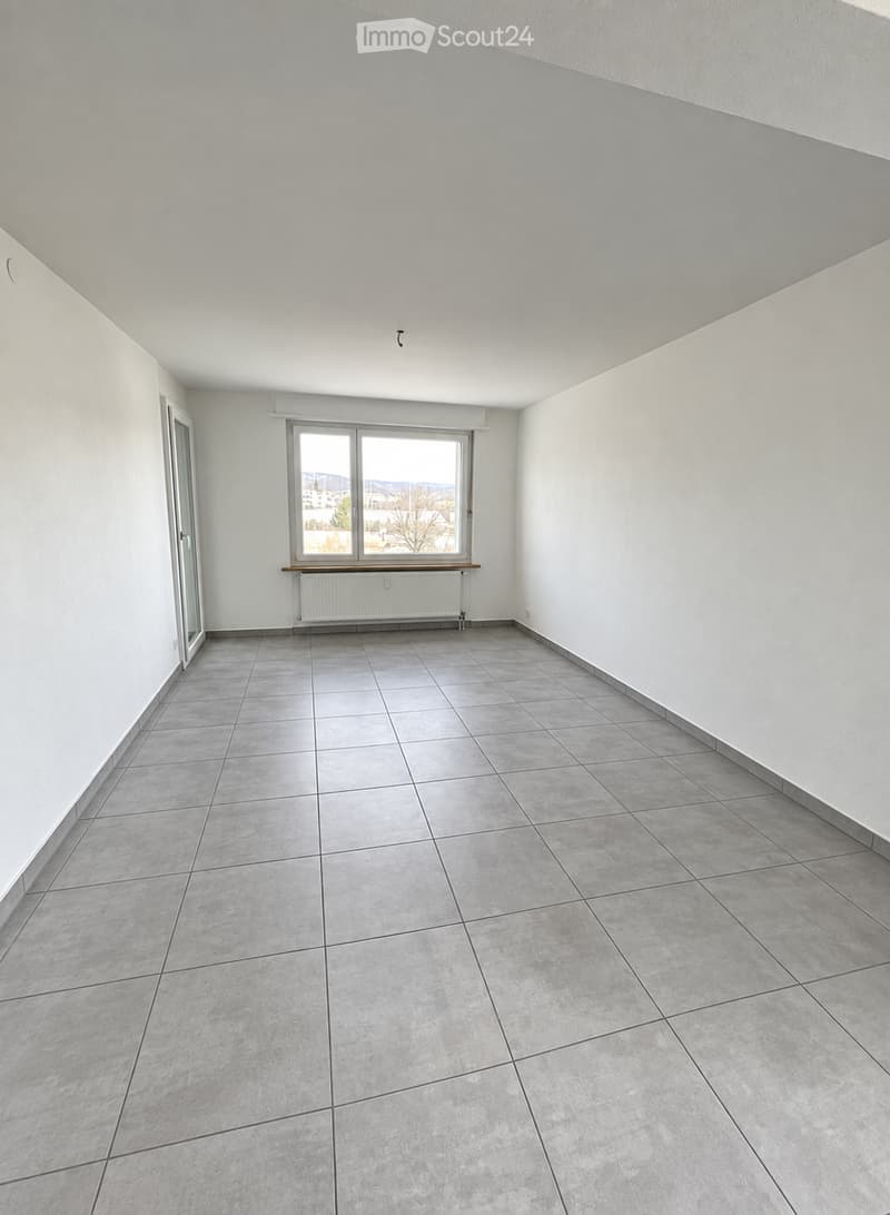 Empty room with tiled floor, white walls, large window, radiator, and door.