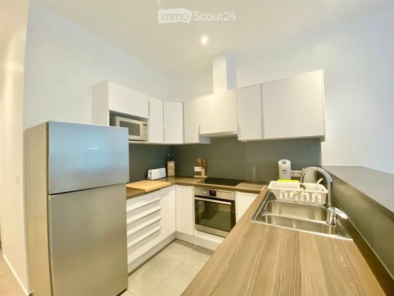Modern kitchen with white cabinets, stainless steel appliances, and a wooden countertop. Features include a refrigerator, microwave, oven, sink, and various small appliances.