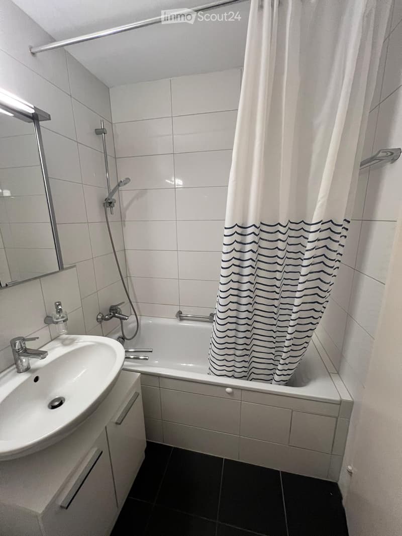 Modern bathroom with white tiles, a sink with a modern faucet, a bathtub with a shower curtain, and a mirror above the sink.