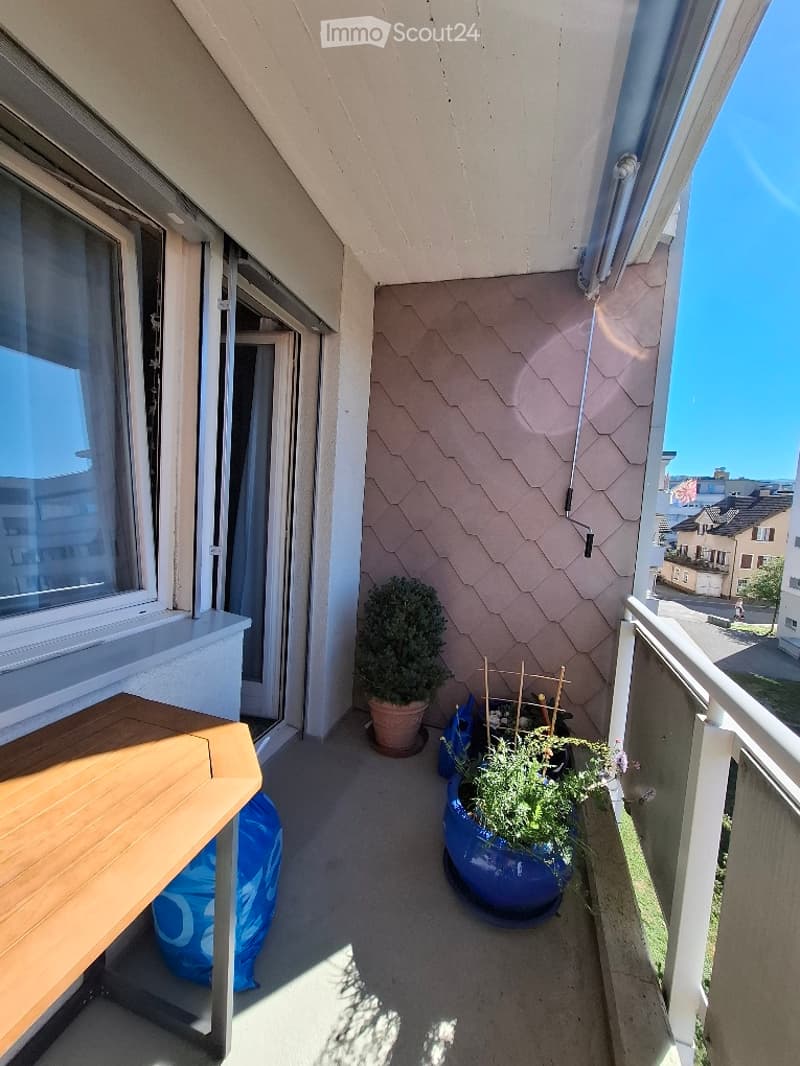 Balcony with wooden table, potted plants, and a view of the street.
