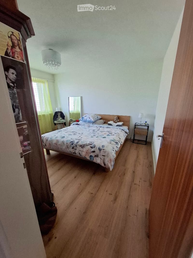 Bedroom with wooden flooring, a bed with a floral duvet, nightstands, a mirror, a chair, and a wardrobe with pictures on it.