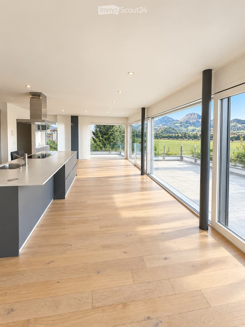 Modern kitchen with light wooden flooring, white cabinetry, and large windows offering a scenic mountain view.