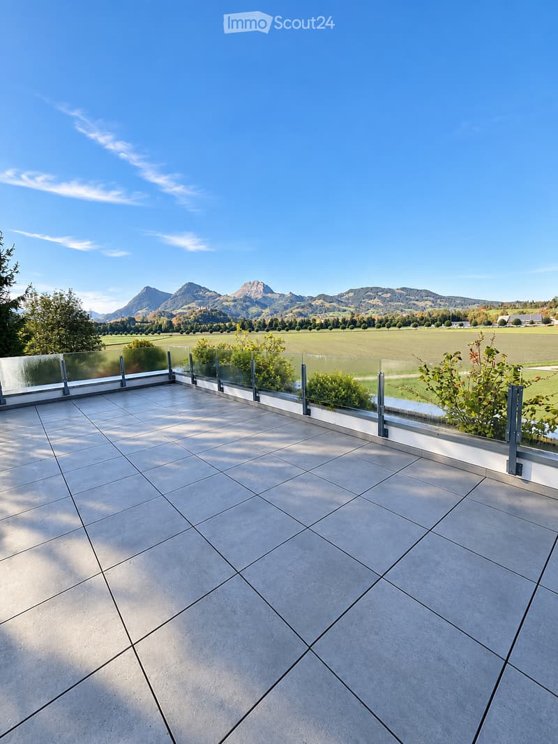 Modern balcony with large glass railing, tiled floor, and scenic mountain view in the background.