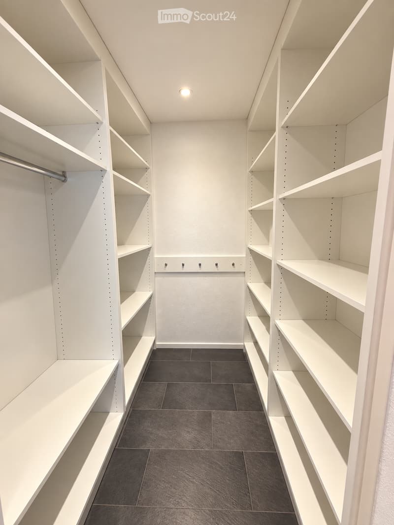 Empty closet with white built-in shelving units and dark tiled floor.