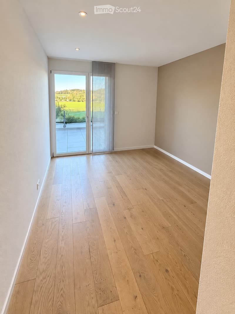 Empty room with light wooden flooring, white walls, and a large sliding glass door leading to an outdoor area.