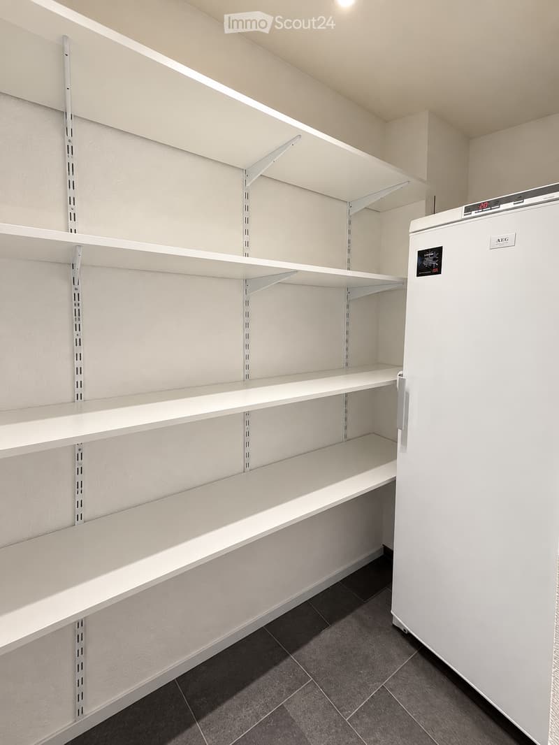 Empty room with white shelving units and a white refrigerator, featuring a dark tiled floor and light-colored walls.