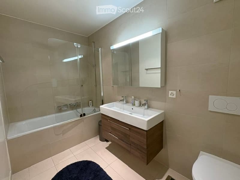 Modern bathroom with a bathtub, double sink, large mirror, and dark wooden cabinetry.