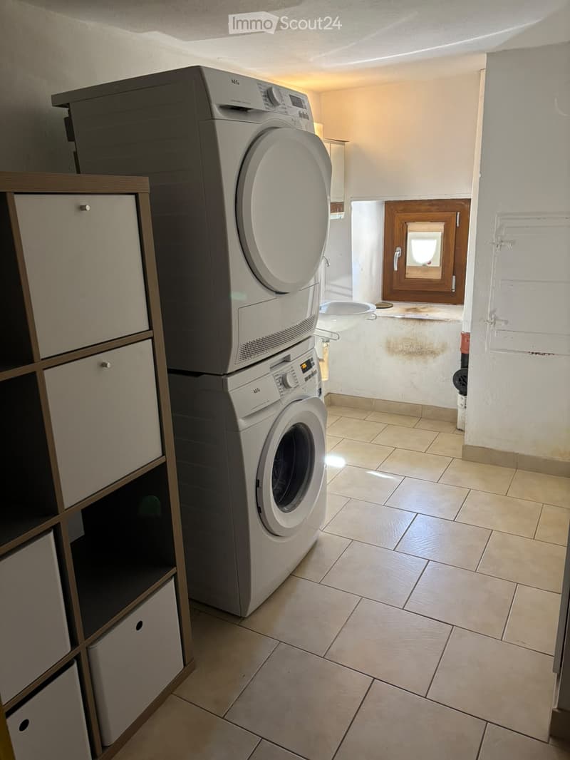 Bathroom with tiled floor, white walls, a washing machine and dryer stacked, and a wooden cabinet with drawers.