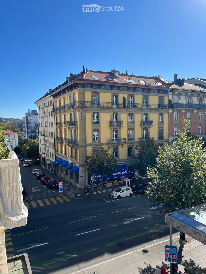 Multi-story building with yellow facade, multiple balconies, and a colorful rooftop mural. The street below shows parked cars and a pedestrian crossing.