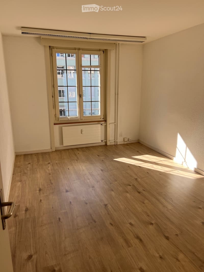 Empty room with wooden flooring, white walls, and a window with a radiator below it.