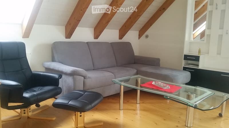 Living room with exposed wooden beams, grey sofa, glass coffee table, black leather chair, and matching ottoman.