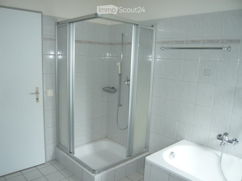 Modern bathroom with a bathtub, glass-enclosed shower, and a sink with a faucet. The walls are tiled, and there is a towel rack on the right side.