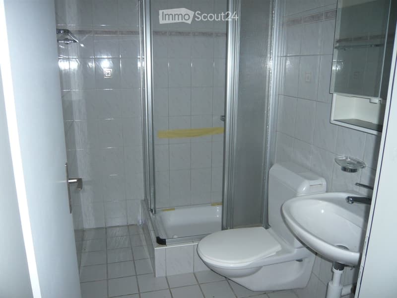Modern bathroom with white tiles, a toilet, a sink, a bathtub, and a mirror. The shower area is enclosed with a glass door.
