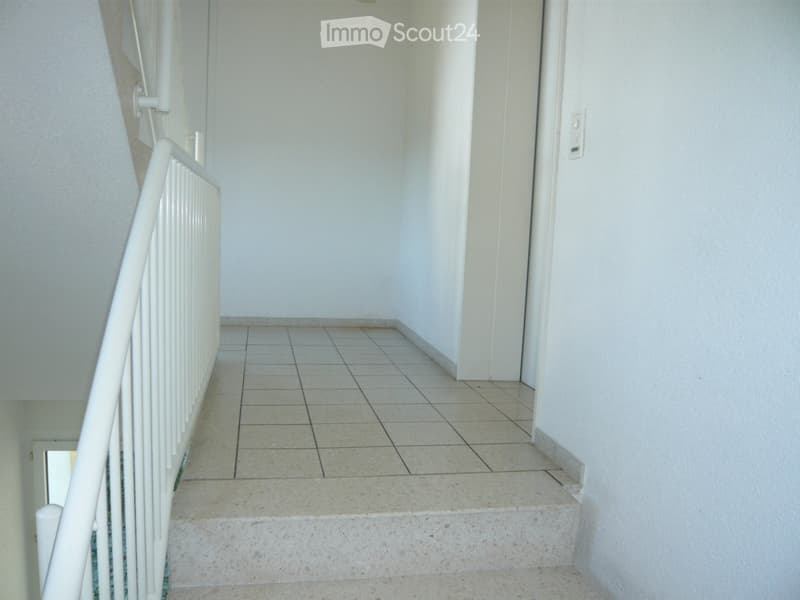 Empty hallway with tiled floor, white walls, and a white staircase railing on the left side.