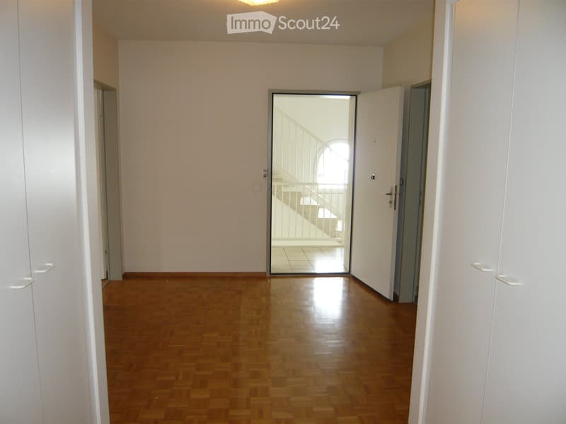 Empty hallway with wooden flooring, white walls, and doors leading to other rooms. A staircase is visible through an open doorway.