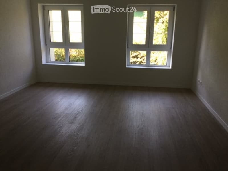 Empty room with wooden flooring and two windows, no furniture or equipment present.