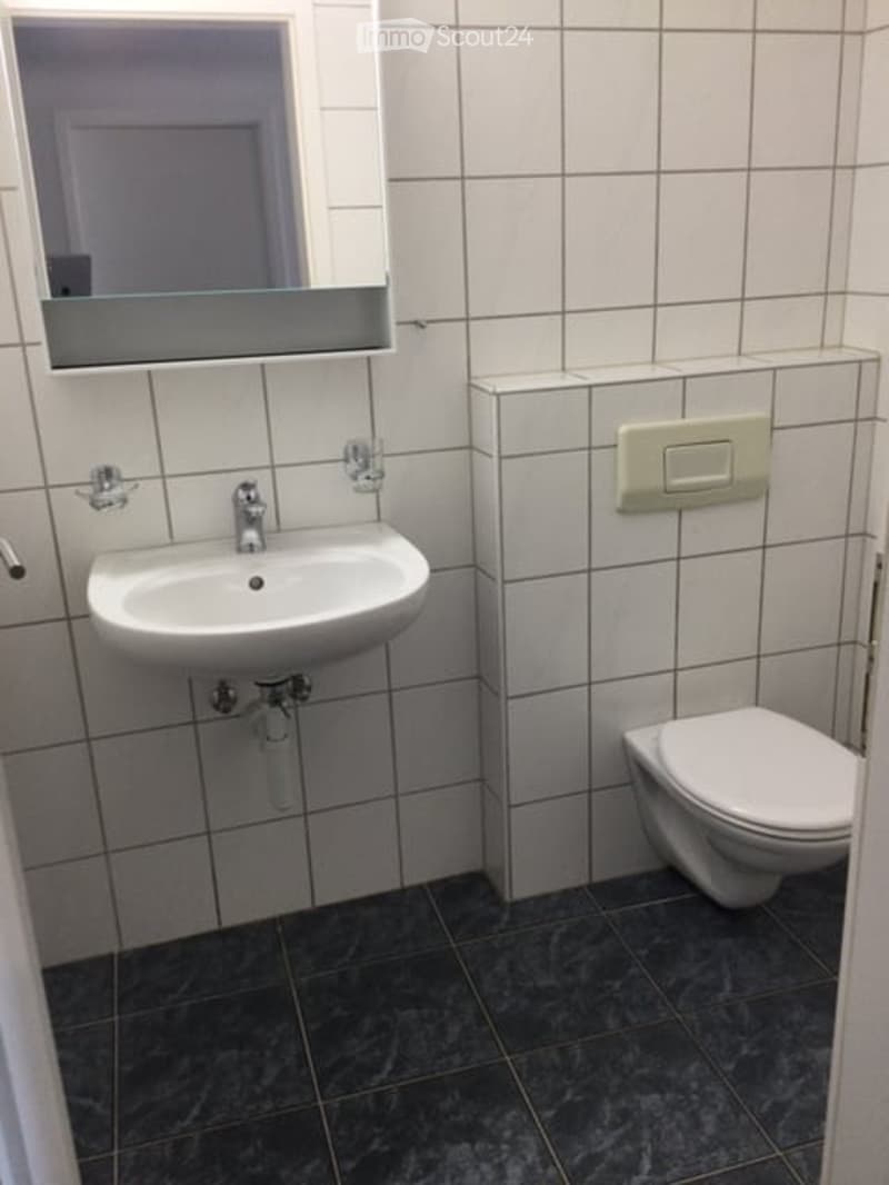 Modern bathroom with white tiled walls, dark grey tiled floor, white sink, toilet, and a mirror above the sink.
