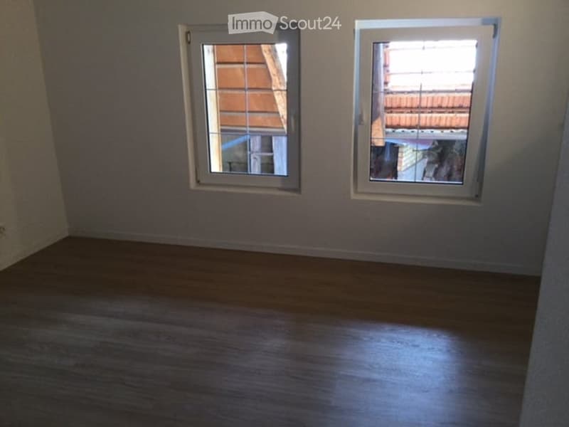 Empty room with wooden flooring and two windows, no furniture or equipment present.