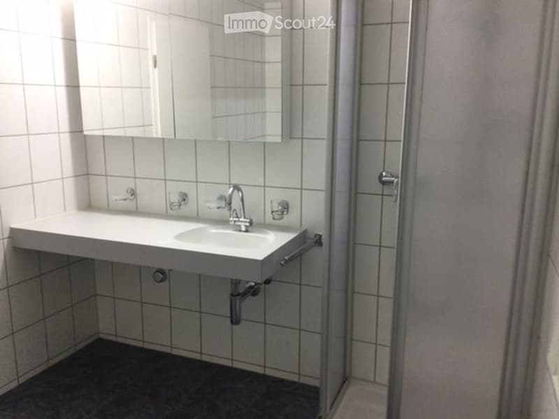 Modern bathroom with white tiled walls, a white sink with a chrome faucet, a large mirror above the sink, and a glass-enclosed shower stall.