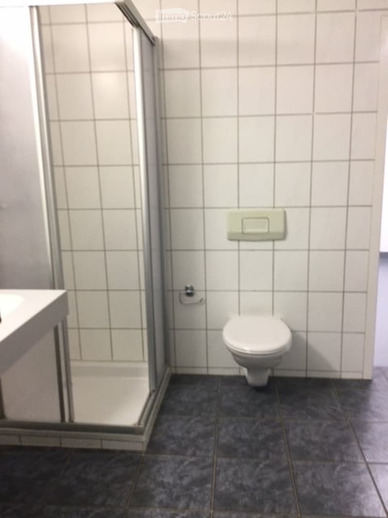 Modern bathroom with white tiled walls, a toilet, and a glass-enclosed shower stall.