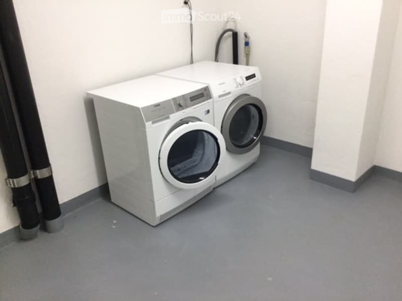 A small, clean utility room with a white washing machine and dryer, grey flooring, and white walls.