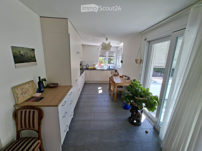 Bright kitchen with white cabinets, a wooden dining table with chairs, a potted plant near the window, and a decorative chair near the counter.