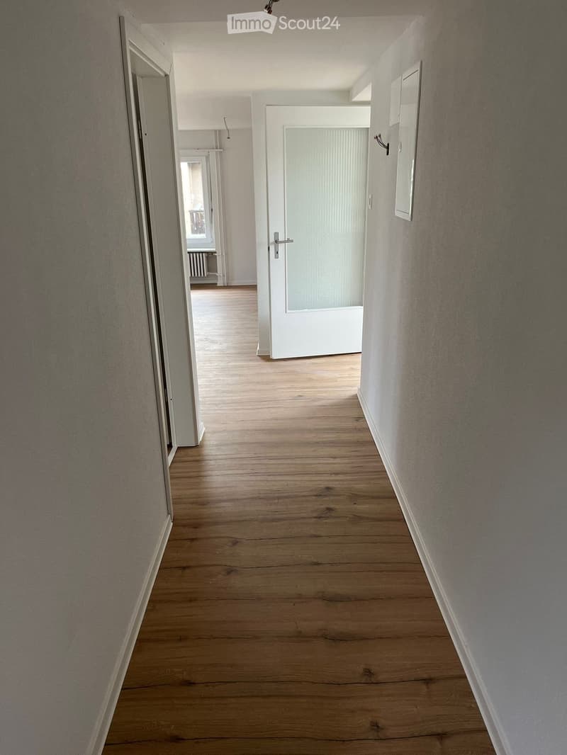 Empty hallway with wooden flooring, white walls, and two doors leading to other rooms.
