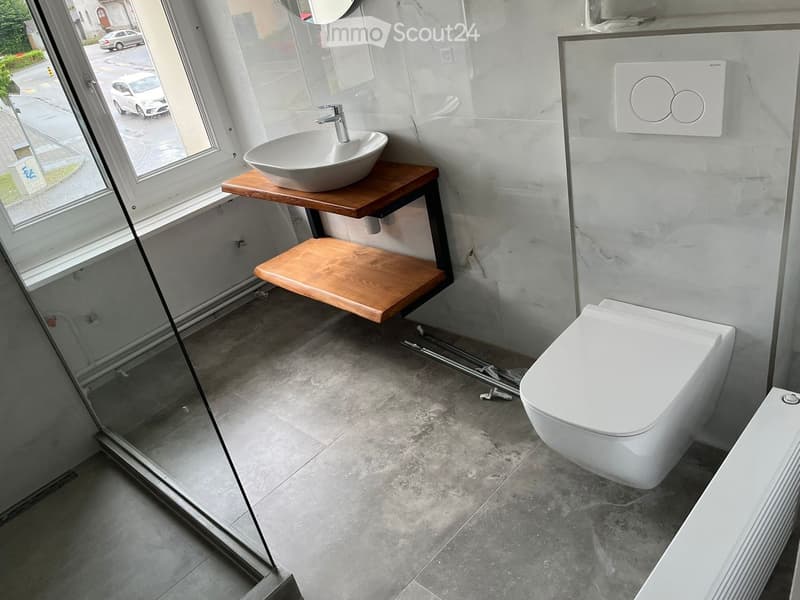Modern bathroom with a floating wooden sink, sleek white toilet, and large window offering a view of the street.