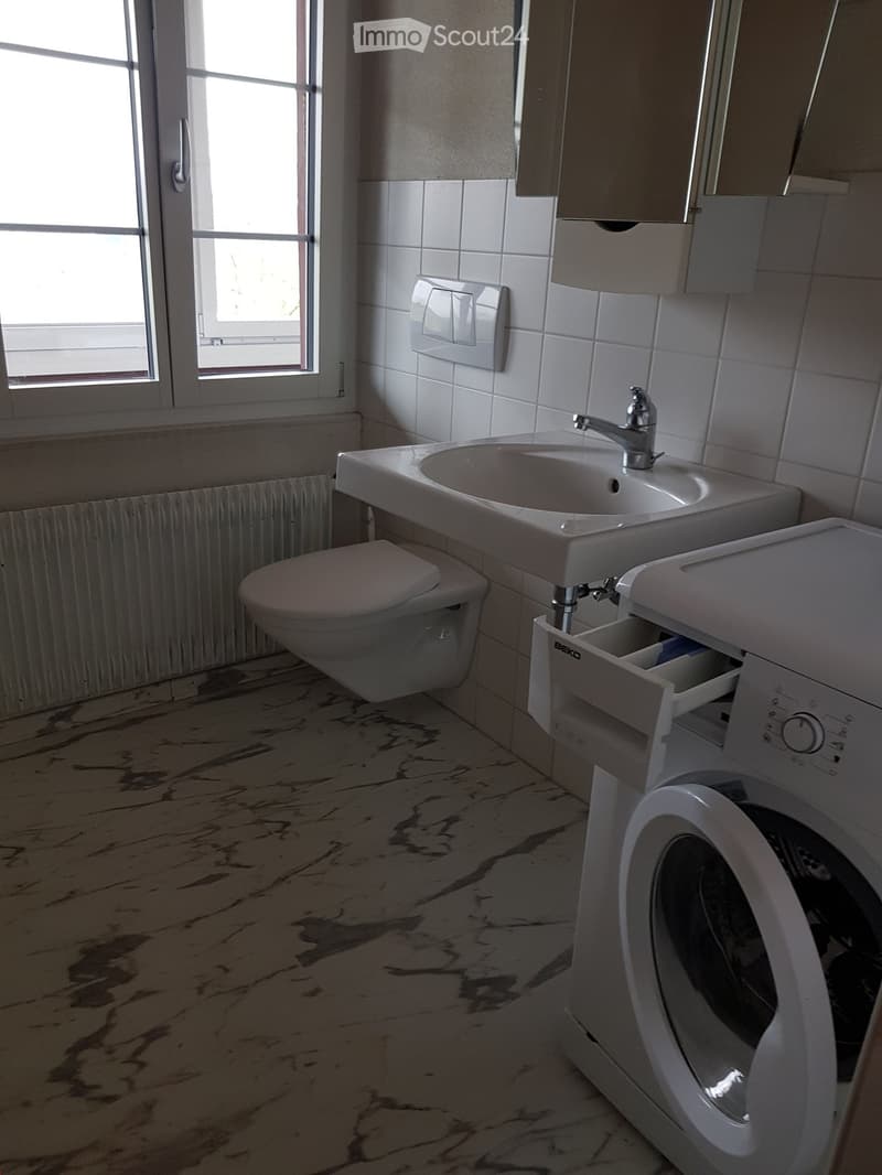 Bathroom with white tiled walls, marble-patterned floor, sink with faucet, toilet, and washing machine.