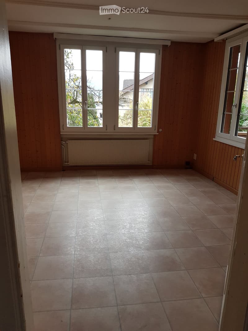 Empty room with tiled floor, wooden panel walls, large sliding glass doors, radiator, and windows.