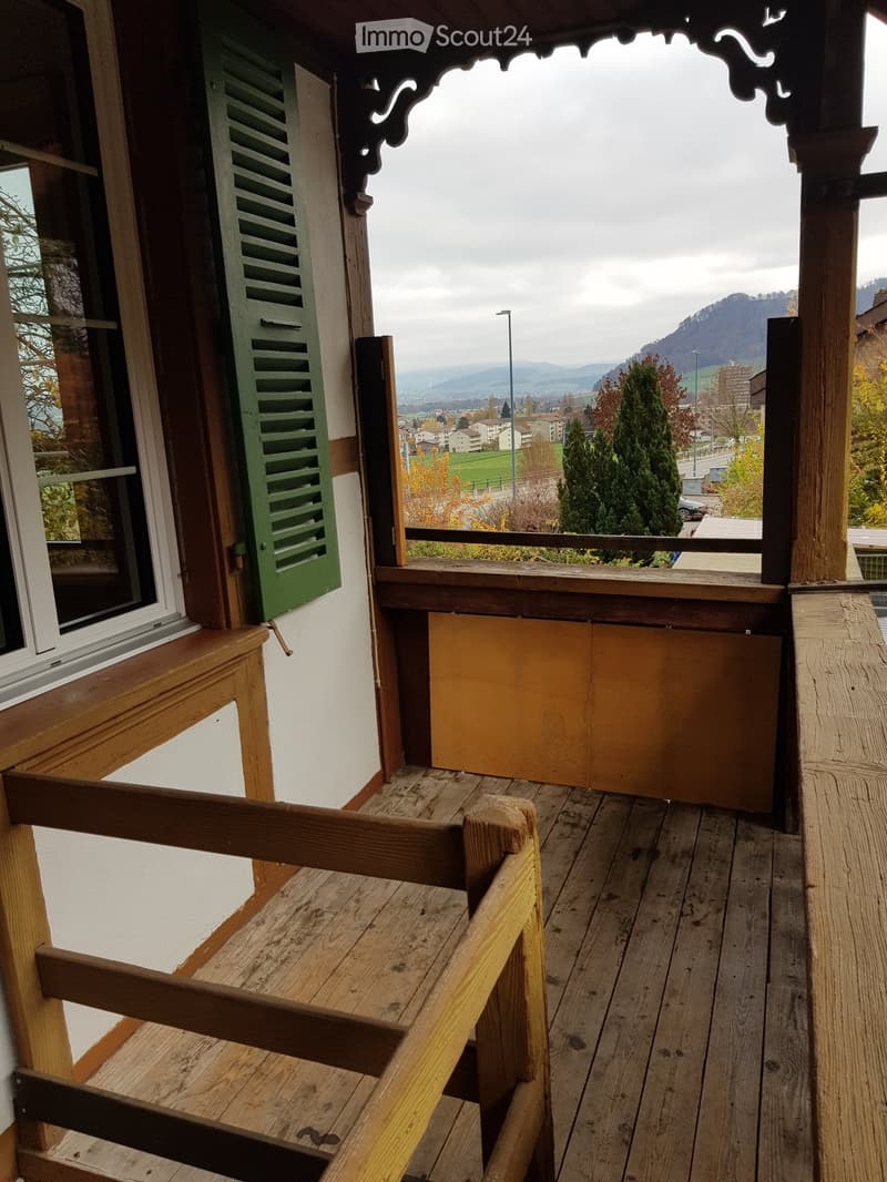 Wooden balcony with ornate wooden railings, green shutters, and a scenic mountain view in the background.